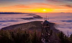 Wieża widokowa na Mogielicy góruje nad morzem chmur podczas zachodu słońca.