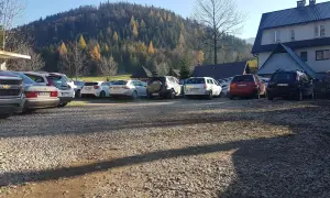 Parking w Kuźnicach, jesienny las na wzgórzu, rząd samochodów na żwirowym placu.