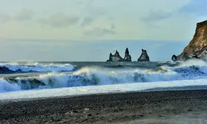 Surowe wybrzeże Islandii, fale rozbijające się o czarny piasek. Wiatr i deszcz mogą wywołać objawy hipotermii na trasach islandzkich.