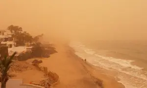 Pomarańczowe niebo i plaża na Wyspach Kanaryjskich, widoczne skutki silnego wiatru calima na szlakach.