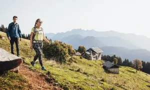 Para idzie szlakiem, co odróżnia wyprawę trekkingową od ekspedycji wysokogórskiej. W tle góry i chatki.
