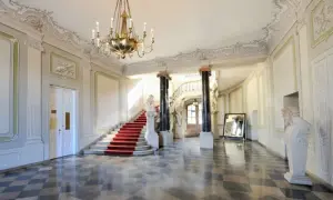 Wnętrze Pałacu Branickich, muzeum. Czerwony dywan na schodach, marmurowa posadzka, żyrandol i rzeźby tworzą elegancką atmosferę.