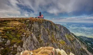 Budynek na szczycie skalistego, trawiastego zbocza górskiego z widokiem na dolinę.