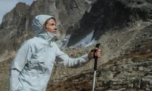 Kobieta w kurtce z membraną Gore-Tex z kijkami trekkingowymi w górach. Czy warto kupować kurtkę z membraną Gore-Tex na letnie wędrówki?