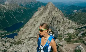 Kobieta w okularach i niebieskim plecaku na tle skalistych gór w Polsce. Widok na jeziora i szczyty.
