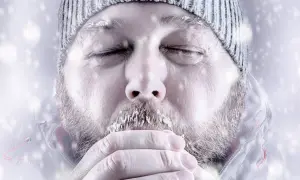 Objawy hipotermii w górach latem: mężczyzna z lodem na brodzie, w czapce i kurtce, z zamkniętymi oczami, ogrzewa dłonie.