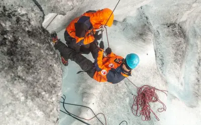 Dwóch alpinistów w pomarańczowych kurtkach wspina się po lodowcu, używając lin i raków.