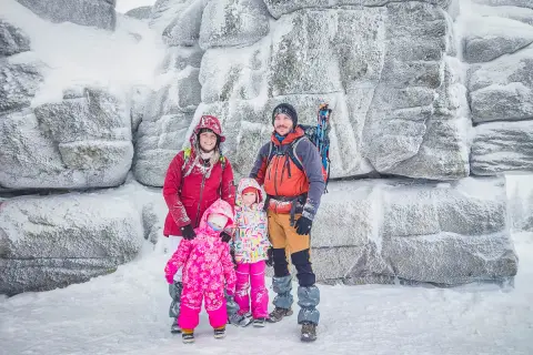 Rodzina w zimowych strojach pozuje na tle ośnieżonych skał na Szrenicy w Szklarskiej Porębie.