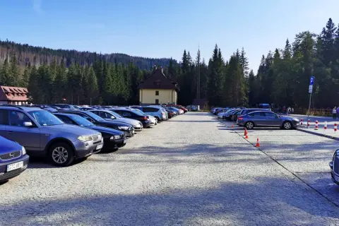 Duży parking przy Palenicy Białczańskiej, pełen samochodów, z górami i lasem w tle.