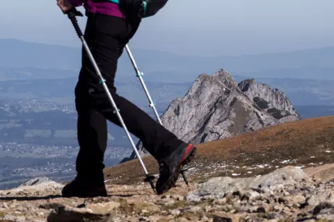 Osoba na szlaku, używająca zbyt krótkich kijków trekkingowych na podejściu, z widokiem na góry i dolinę.