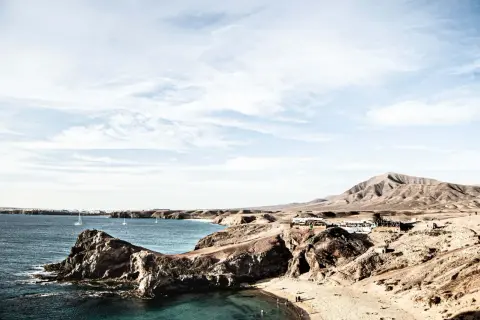 Surowe krajobrazy wulkaniczne Lanzarote, gdzie skutki braku zapasu wody są widoczne na trasach turystycznych, kontrastują z błękitem oceanu i białymi żaglami.