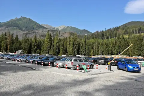 Duży, kamienisty morskie oko parking pełen samochodów, otoczony gęstym lasem świerkowym i górami.