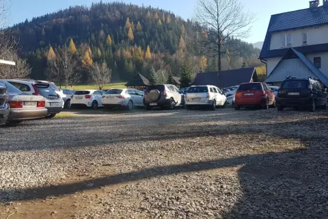 Parking w Kuźnicach, jesienny las na wzgórzu, rząd samochodów na żwirowym placu.