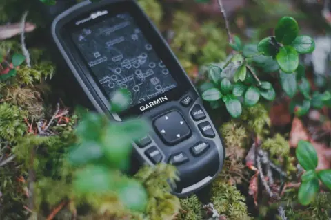 Garmin inReach, jako akcesoria do komunikacji satelitarnej, leży na mchu w lesie.