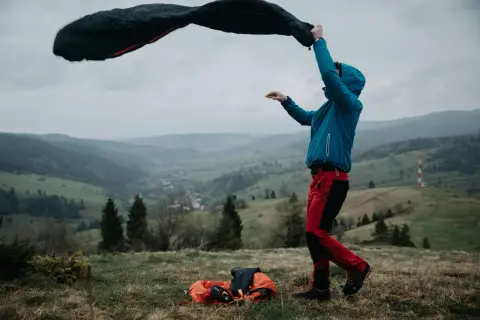 Mężczyzna rozkłada śpiwór na tle gór. Wybór między śpiworem puchowym a syntetycznym na nocleg w schronisku zależy od warunków.