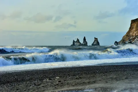 Surowe wybrzeże Islandii, fale rozbijające się o czarny piasek. Wiatr i deszcz mogą wywołać objawy hipotermii na trasach islandzkich.
