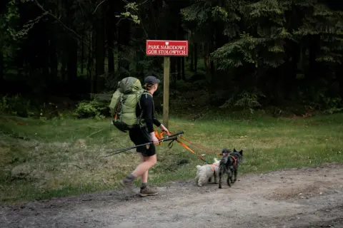 Czy można przejść szlak z psem? Przepisy parków narodowych 2026. Turystka z plecakiem i dwoma psami na smyczy w Parku Narodowym Gór Stołowych.