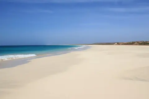 Pusta, piaszczysta plaża z turkusową wodą i błękitnym niebem.