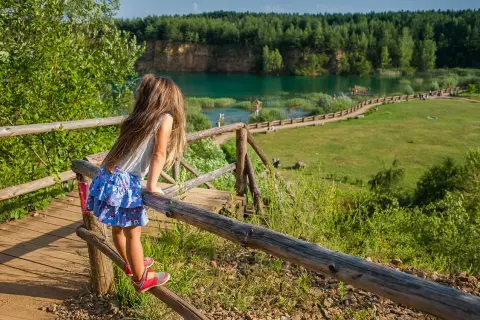 Dziewczynka na drewnianej kładce podziwia turkusową wodę i zieleń. To polskie Malediwy w Jaworznie, idealne miejsce na letni relaks.