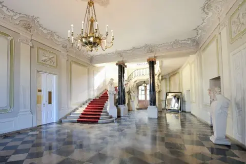 Wnętrze Pałacu Branickich, muzeum. Czerwony dywan na schodach, marmurowa posadzka, żyrandol i rzeźby tworzą elegancką atmosferę.