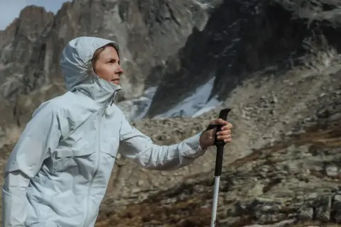 Kobieta w kurtce z membraną Gore-Tex z kijkami trekkingowymi w górach. Czy warto kupować kurtkę z membraną Gore-Tex na letnie wędrówki?