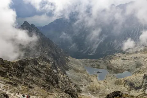 Widok na Tatry Wysokie, z mgłą spowijającą szczyty. Widoczna ścieżka i jeziorka. Planowanie wejścia na Rysy od strony słowackiej i polskiej wymaga dobrej kondycji.