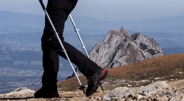 Osoba na szlaku, używająca zbyt krótkich kijków trekkingowych na podejściu, z widokiem na góry i dolinę.