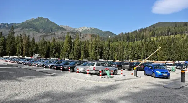 Duży, kamienisty morskie oko parking pełen samochodów, otoczony gęstym lasem świerkowym i górami.