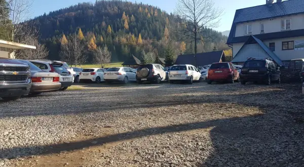 Parking w Kuźnicach, jesienny las na wzgórzu, rząd samochodów na żwirowym placu.