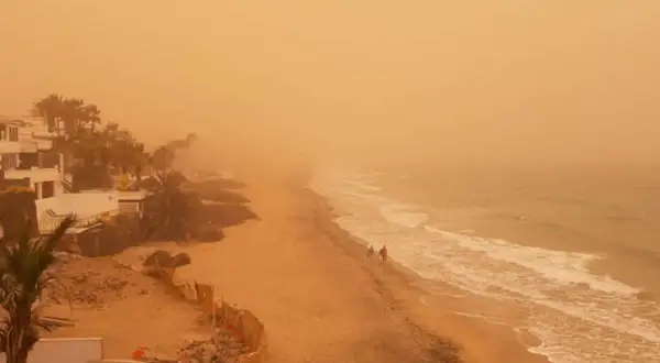 Pomarańczowe niebo i plaża na Wyspach Kanaryjskich, widoczne skutki silnego wiatru calima na szlakach.