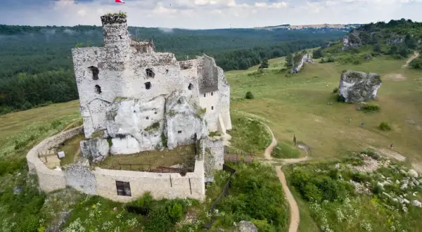 Ruiny zamku w Mirowie, majestatycznie wznoszące się na skale, otoczone zielenią i wapiennymi ostańcami.