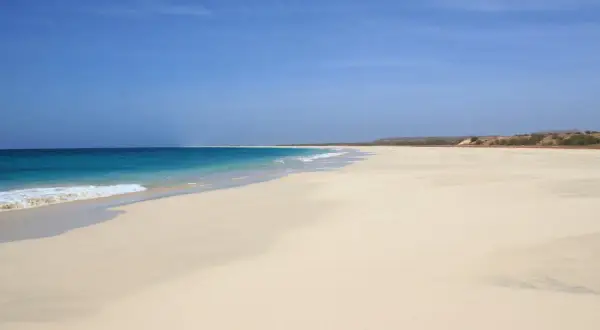 Pusta, piaszczysta plaża z turkusową wodą i błękitnym niebem.