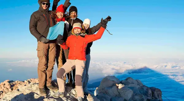 Grupa przyjaciół na szczycie wulkanu Teide, ciesząca się widokiem. Wejście na wulkan Teide zajmuje kilka godzin i wymaga zezwolenia.