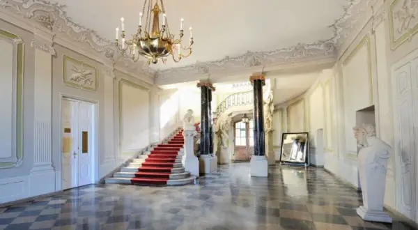 Wnętrze Pałacu Branickich, muzeum. Czerwony dywan na schodach, marmurowa posadzka, żyrandol i rzeźby tworzą elegancką atmosferę.