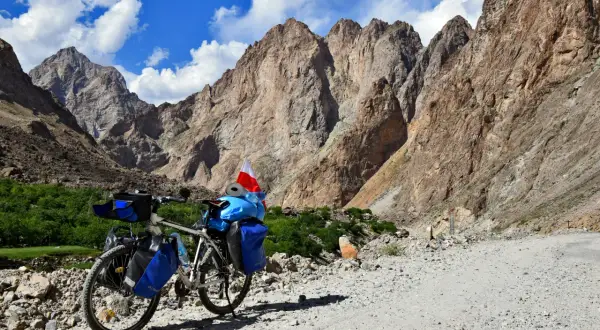 Rower z sakwami i polską flagą na tle gór Pamiru. To inspiracja, jak zaplanować logistykę wyprawy rowerowej przez Pamir Highway.