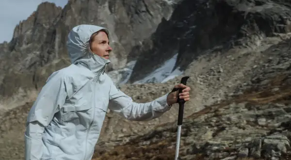 Kobieta w kurtce z membraną Gore-Tex z kijkami trekkingowymi w górach. Czy warto kupować kurtkę z membraną Gore-Tex na letnie wędrówki?