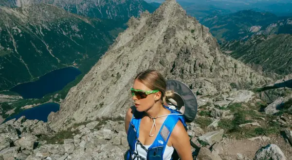 Kobieta w okularach i niebieskim plecaku na tle skalistych gór w Polsce. Widok na jeziora i szczyty.