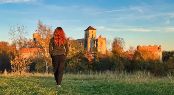 Kobieta z rudymi włosami idzie w stronę ruin zamku. To krajobraz inny niż krakowskie kopce, ale równie piękny jak trasy w Jurze Krakowsko-Częstochowskiej.
