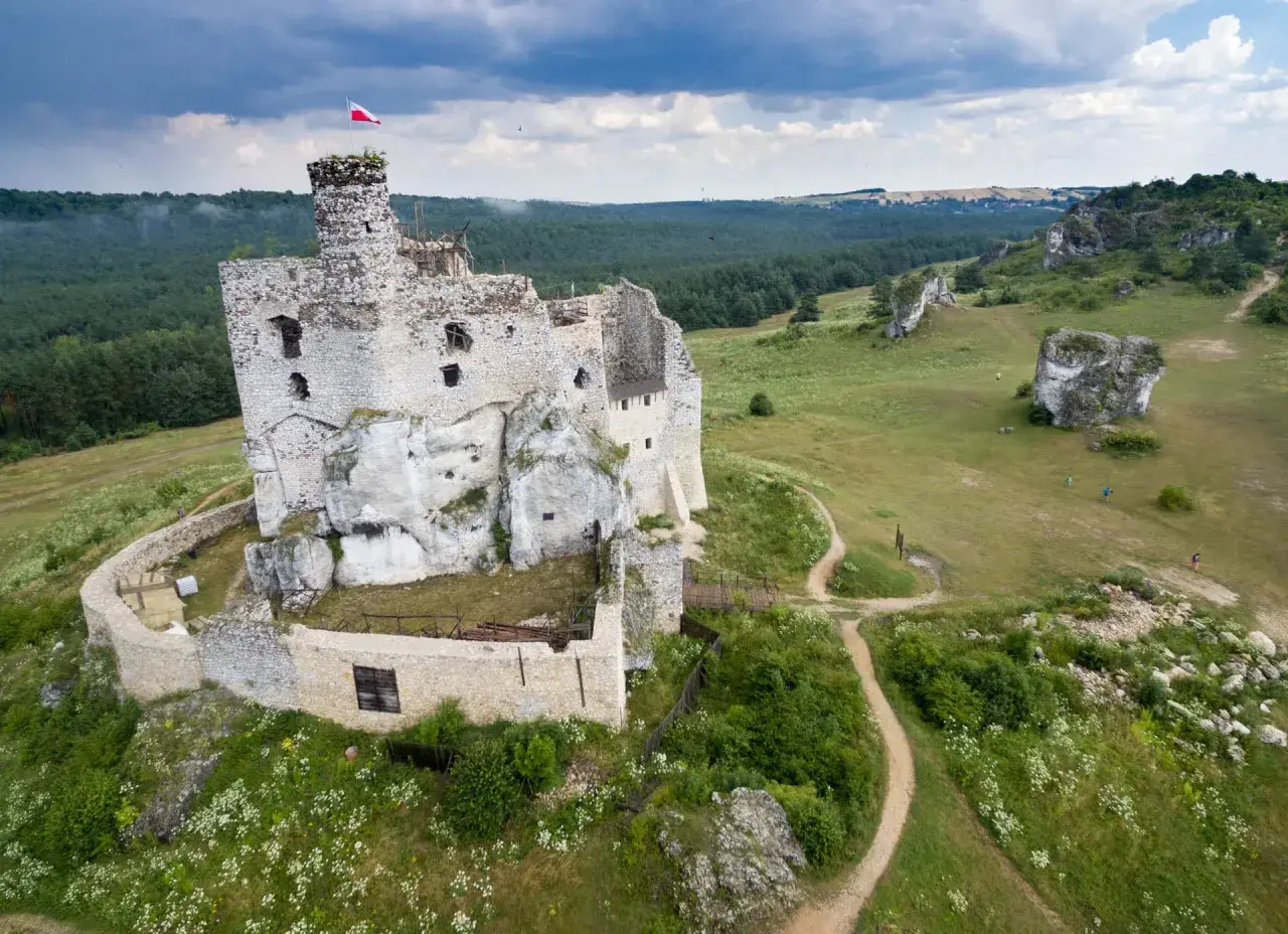 Ruiny zamku w Mirowie, majestatycznie wznoszące się na skale, otoczone zielenią i wapiennymi ostańcami.