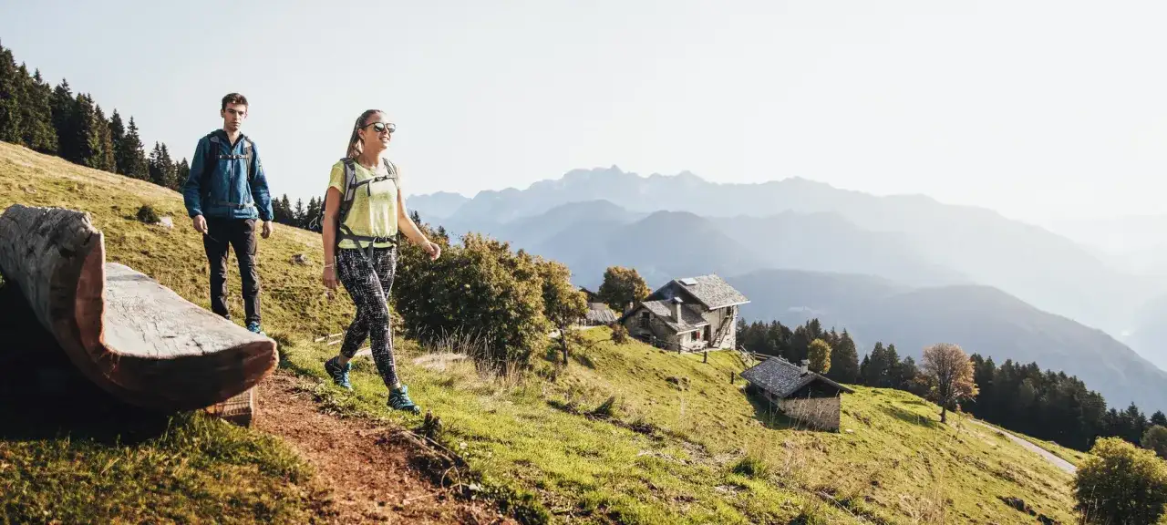 Para idzie szlakiem, co odróżnia wyprawę trekkingową od ekspedycji wysokogórskiej. W tle góry i chatki.