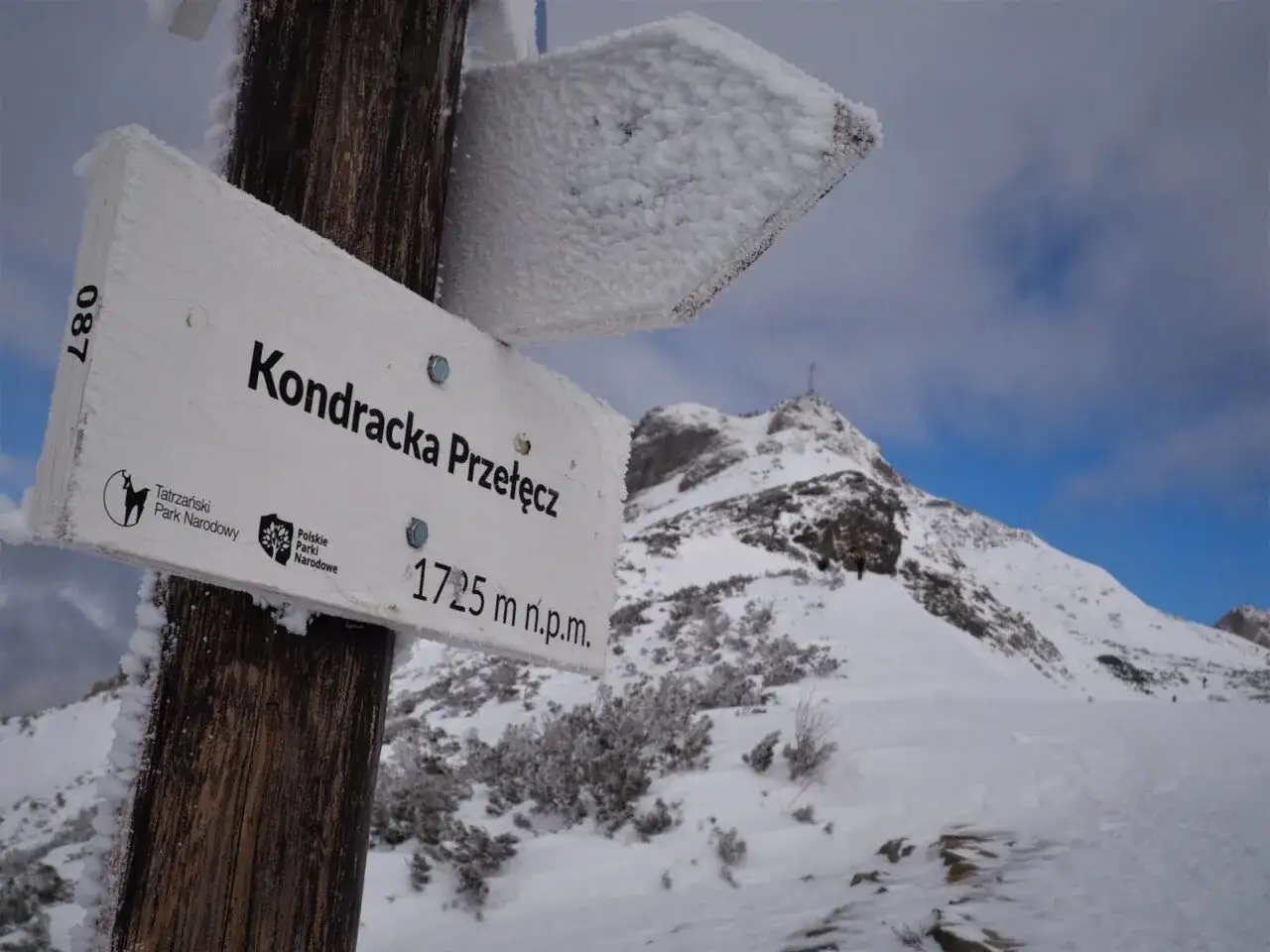 Znak wskazuje Kondracką Przełęcz (1725 m n.p.m.), symbolizując różnicę między wejściem na szczyt a przejściem przez przełęcz.