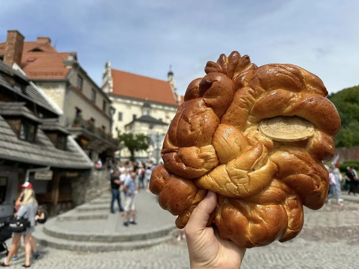 Złocisty, pleciony chleb z opłatkiem, symbol kazimierz dolny atrakcje. W tle urokliwa zabudowa i spacerujący turyści.