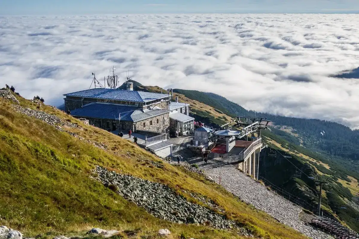 Widok z Kasprowego Wierchu, którego wysokość zachwyca, na morze chmur i budynki górnej stacji kolejki.