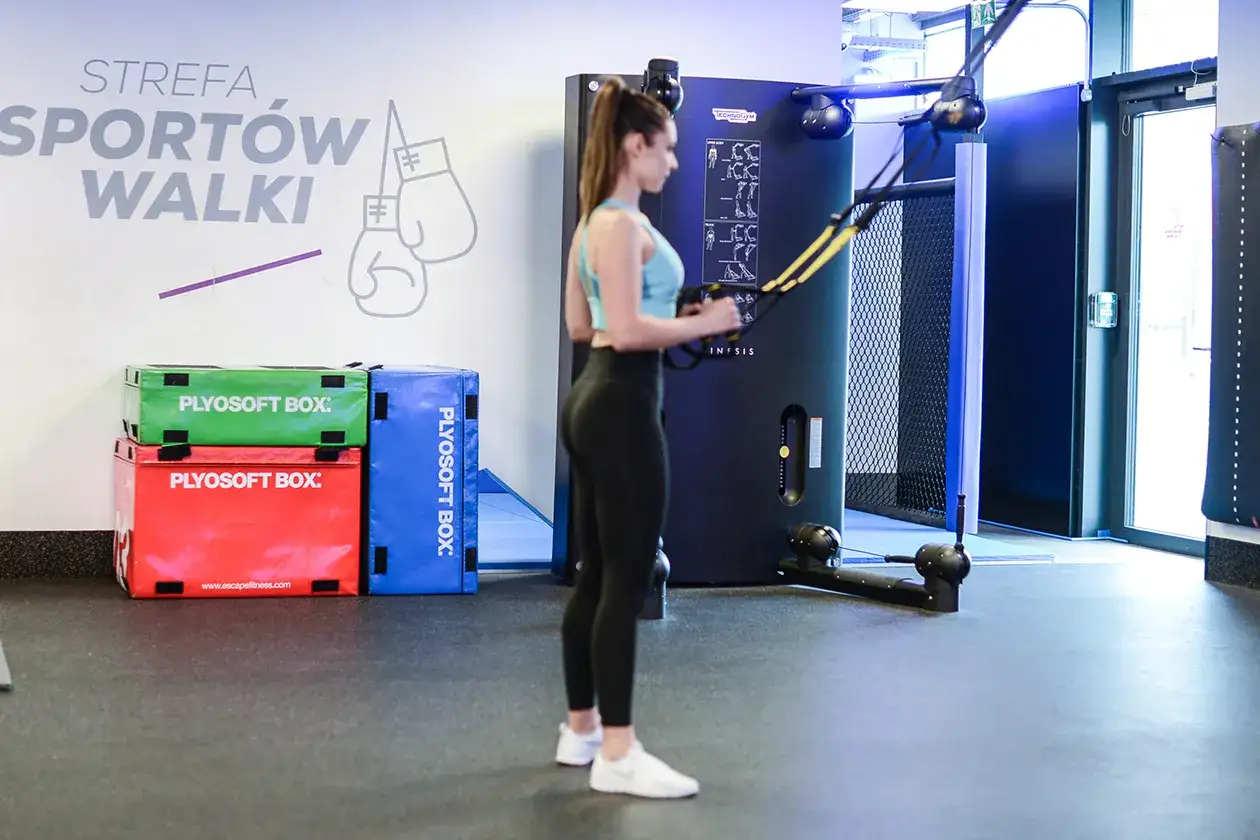 Kobieta ćwiczy na TRX, przygotowując kondycję do wyprawy w góry wysokie bez siłowni. Obok skrzynie plyo.