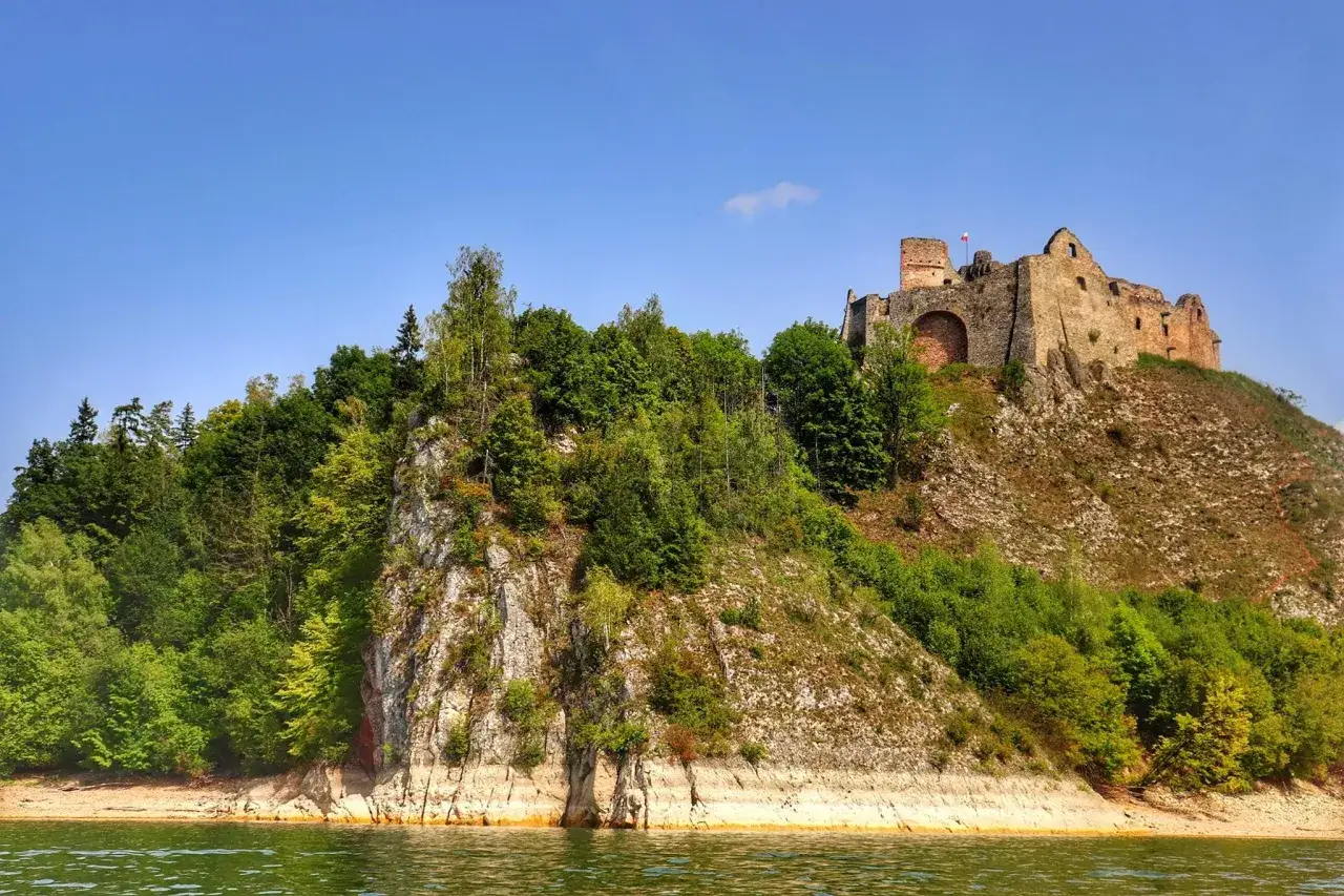 Zamek w Czorsztynie góruje nad jeziorem, otoczony zielenią. Ruiny zamku na skale, widok z wody.