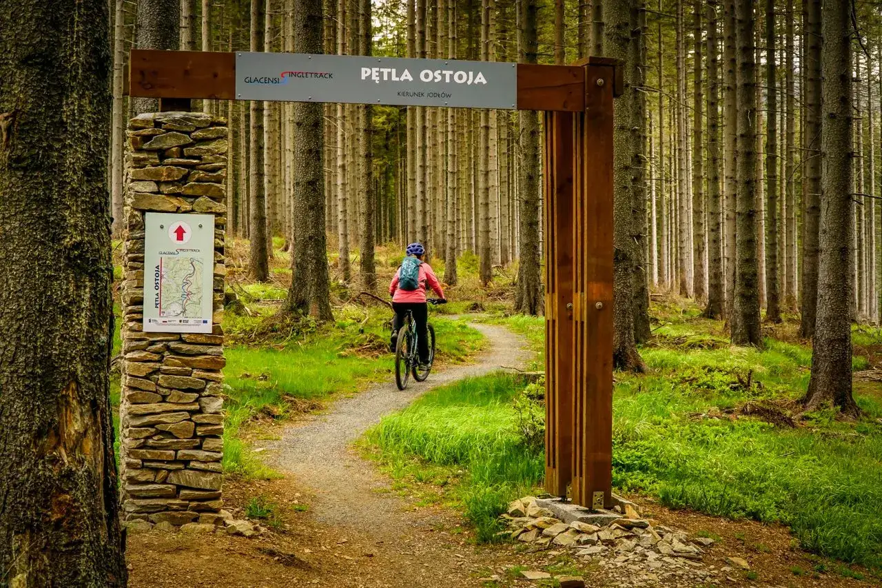 Rowerzystka na singletracku Glacensis. Mapa wskazuje różnicę między trasą turystyczną a rowerową.