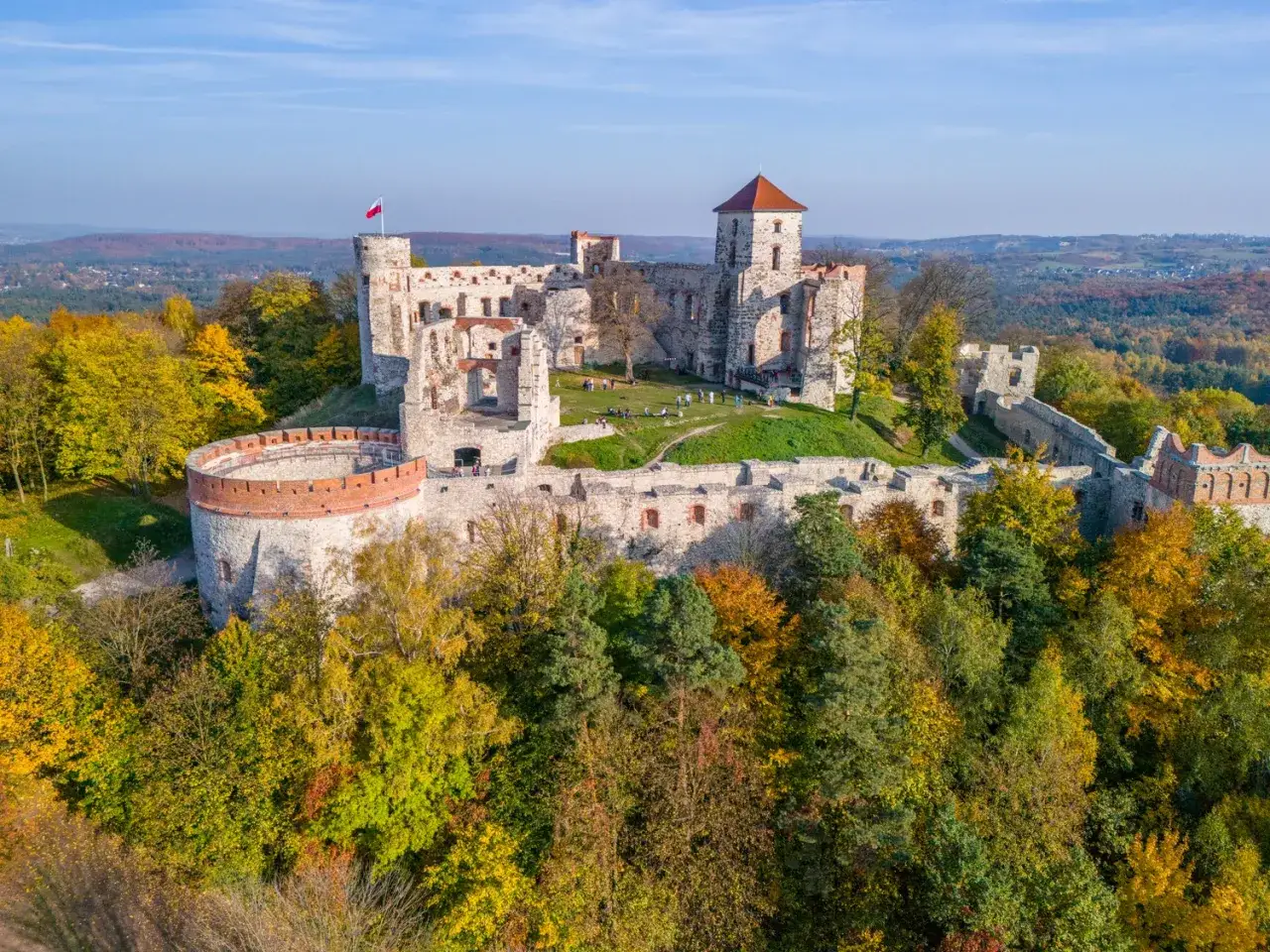 Jesienne słońce oświetla ruiny zamku w Mirowie, otoczone kolorowymi drzewami.