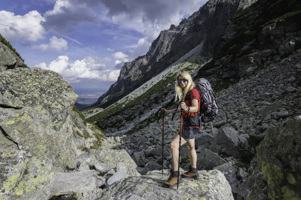 Kobieta z plecakiem i kijkami trekkingowymi na kamienistym szlaku. Warto wiedzieć, jakie trasy w słowackich Tatrach wymagają dodatkowego ubezpieczenia.