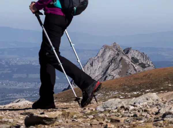 Osoba na szlaku, używająca zbyt krótkich kijków trekkingowych na podejściu, z widokiem na góry i dolinę.