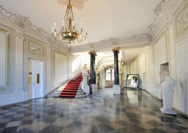 Wnętrze Pałacu Branickich, muzeum. Czerwony dywan na schodach, marmurowa posadzka, żyrandol i rzeźby tworzą elegancką atmosferę.